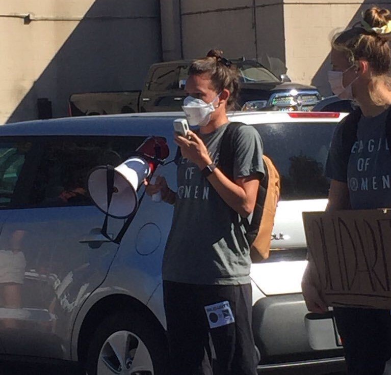 Emily Menges speaks into a bullhorn. To her left, Bella Bixby holds a sign reading "Solidarity".